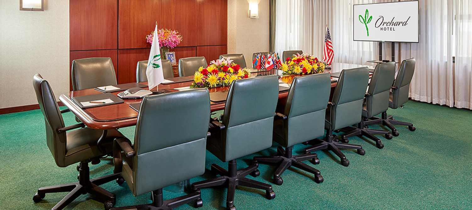a conference room with a long table, chairs, flowers, flags, and a screen