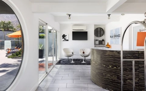 A modern hotel lobby with a reception desk, seating area, and a TV on the wall.