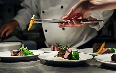 A chef placing a slice of yellow pepper on a plate of food.