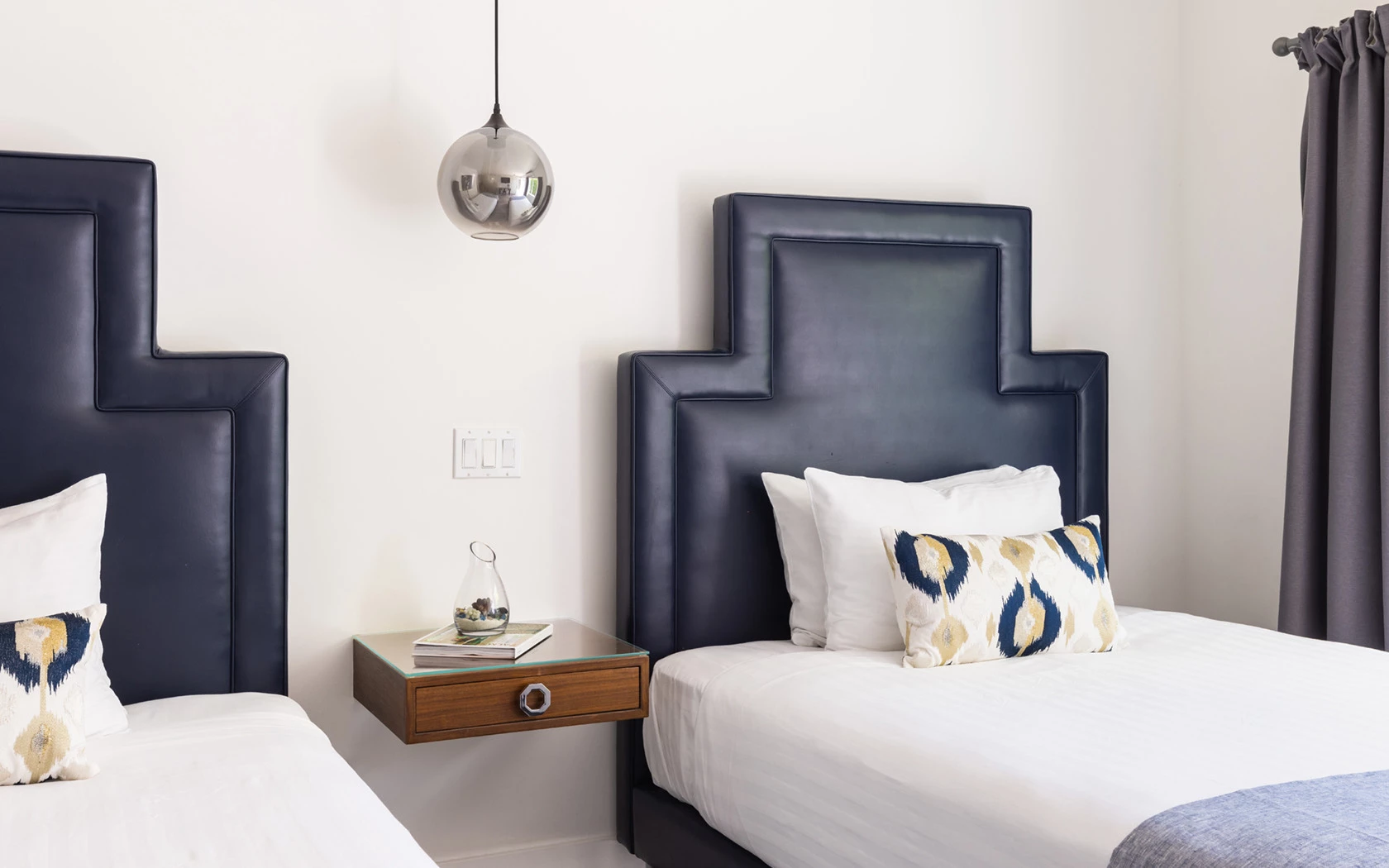 A hotel room with two twin beds, a nightstand, and a pendant light.