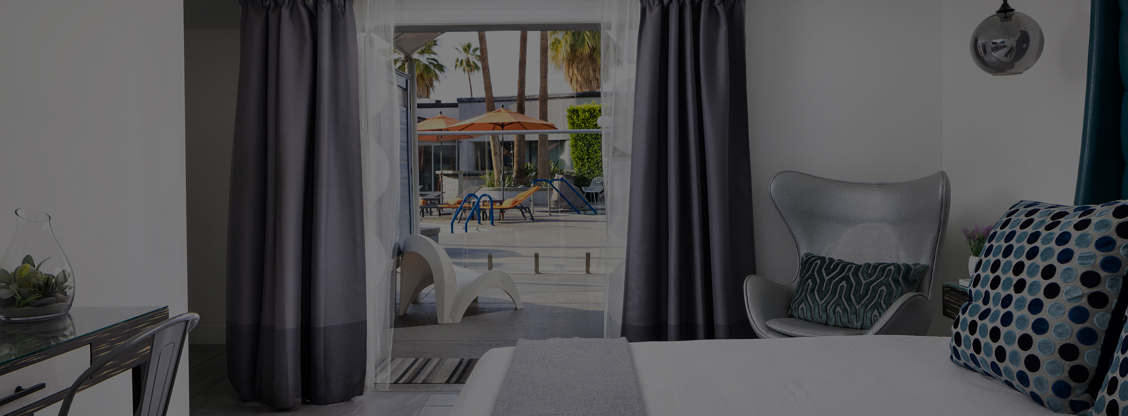 A hotel room with a bed, chair, desk, and window overlooking the pool area.
