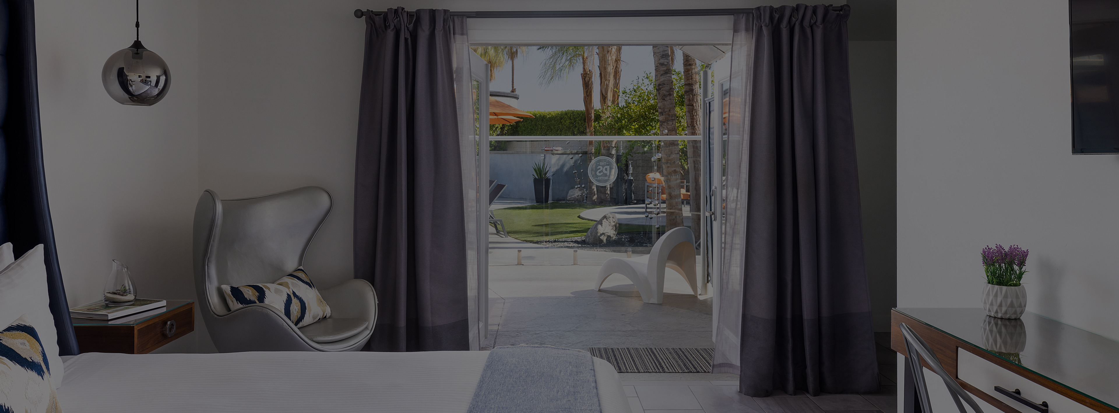 A wide view of a hotel room with a bed, chair, desk, and sliding glass door leading to an outdoor patio.