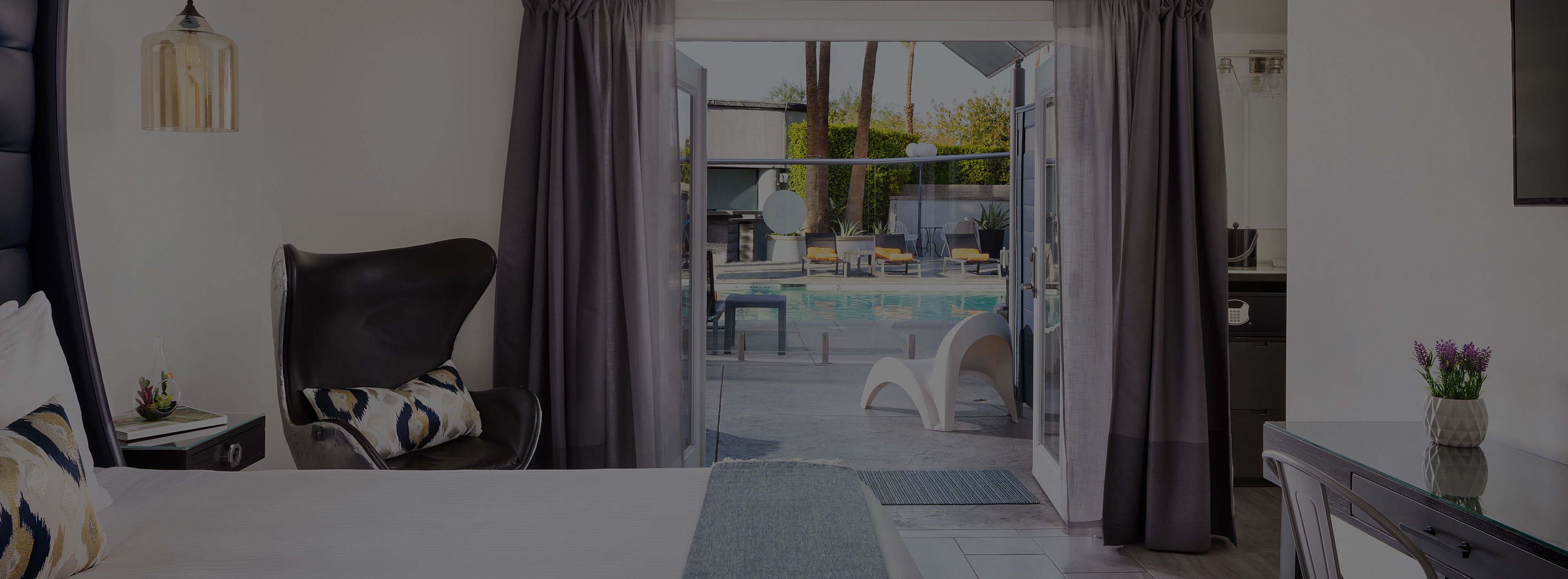 A wide view of a hotel room with a bed, chair, desk, and door leading to a patio with a pool.