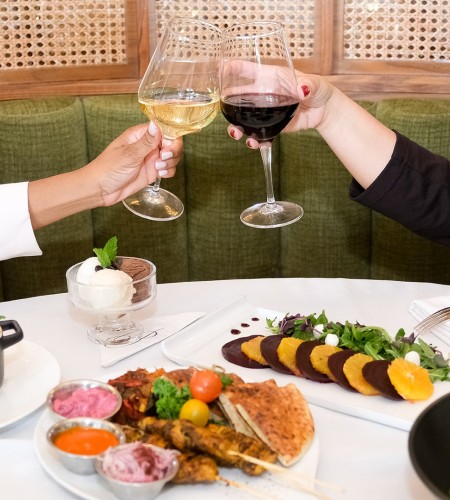 a pair of hands holding wine glasses at a table with food