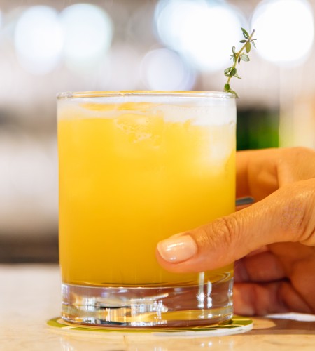 a hand holding a glass of yellow liquid