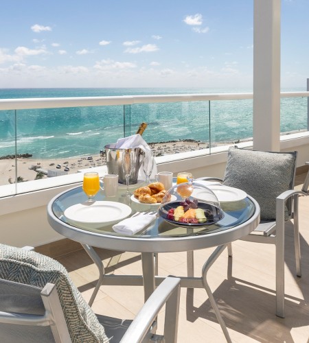 a table with food on it and chairs on a balcony overlooking the ocean