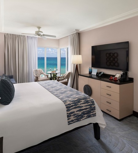 A wide-angle view of a hotel room with a large bed, flat-screen TV, and ocean view.