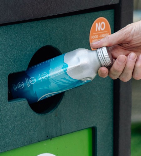 a hand holding a bottle into a trash can