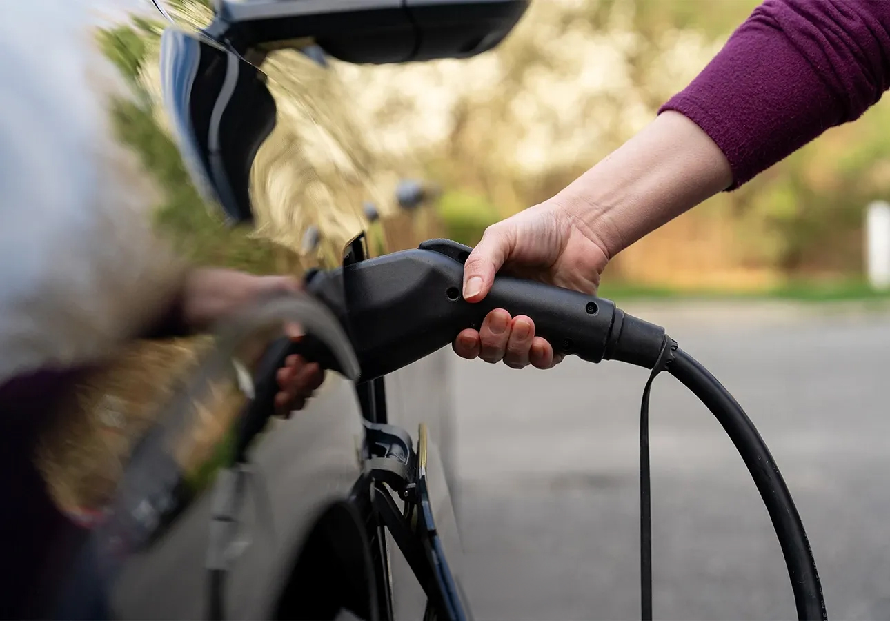 a person holding a black cable to a car