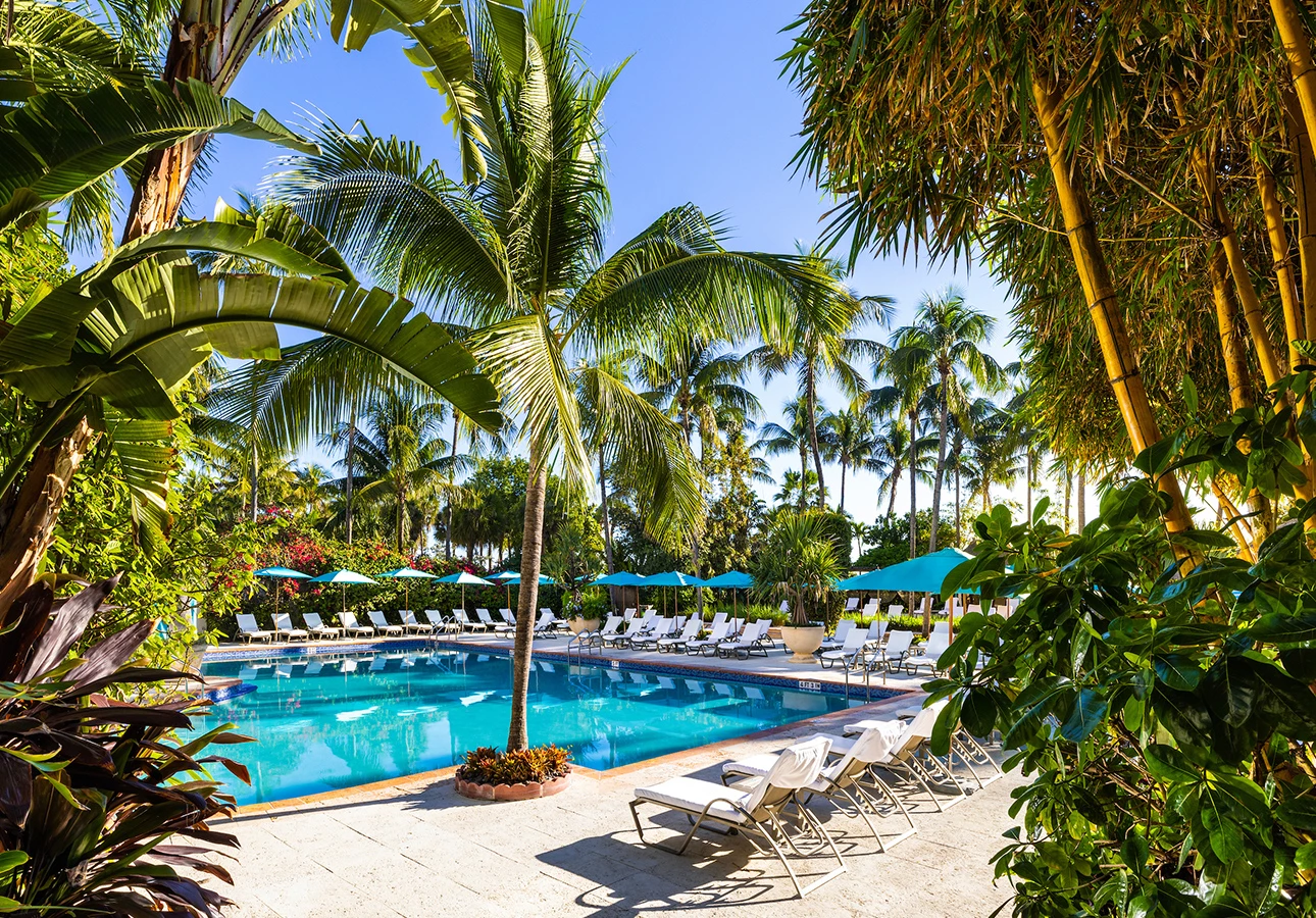 A serene poolside scene with white lounge chairs, turquoise umbrellas, and palm trees.