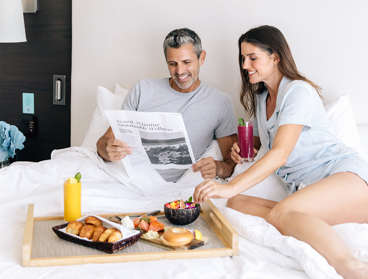 a man and woman sitting in bed with breakfast