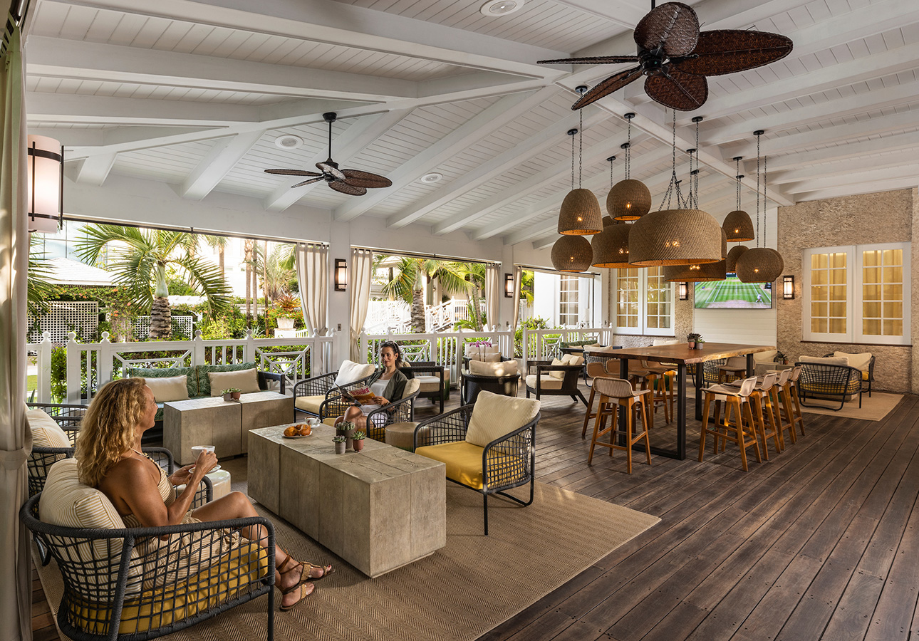 a group of people sitting in chairs and tables in a room with a ceiling fan