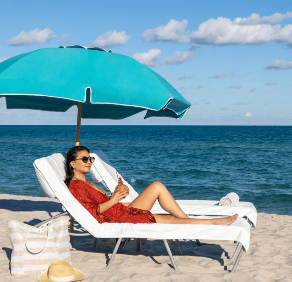 a woman sitting on a beach chair under a blue umbrella