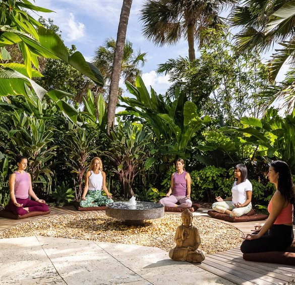 a group of people sitting in lotus position in a circle with trees and a fountain