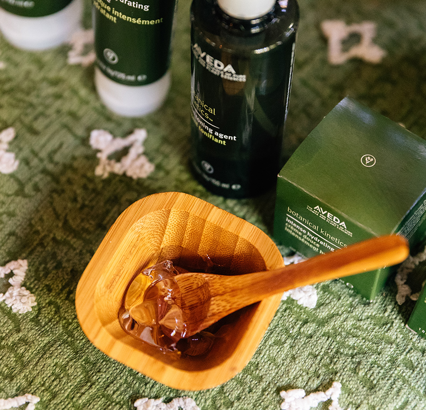 a wooden bowl with a wooden spoon in it next to a container of hair gel
