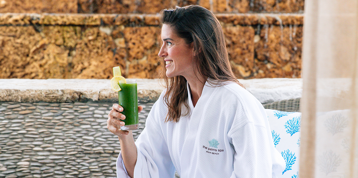 a woman in a white robe holding a green drink