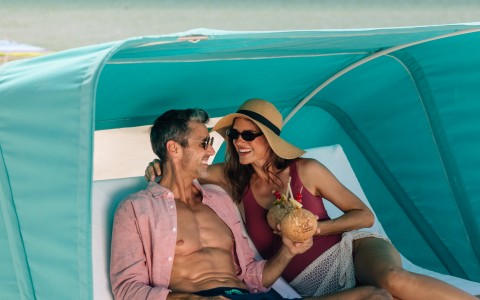 a man and woman sitting on a bed with a drink