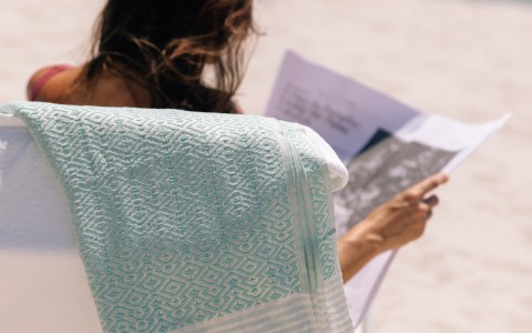 a woman sitting in a chair reading a magazine on the beach
