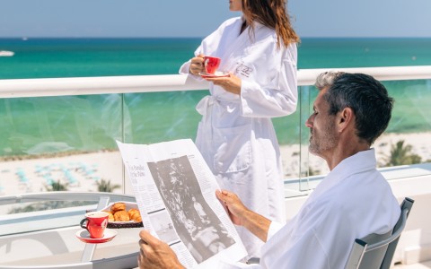 a man and woman in white robes on a balcony overlooking the ocean