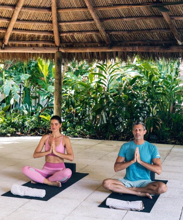 a man and woman meditating under a straw roof