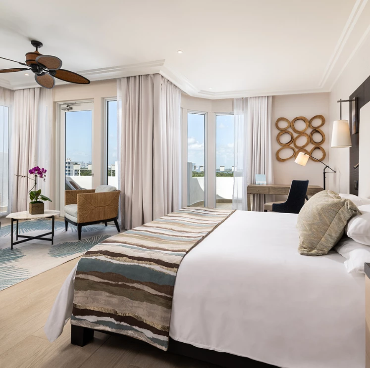 A wide view of a hotel room with a large bed, desk, chair, and balcony
