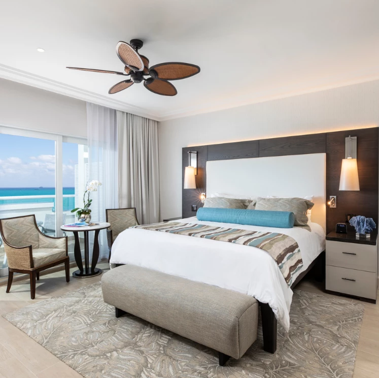 A wide-angle view of a modern hotel room with a large bed, ocean view, and seating area.