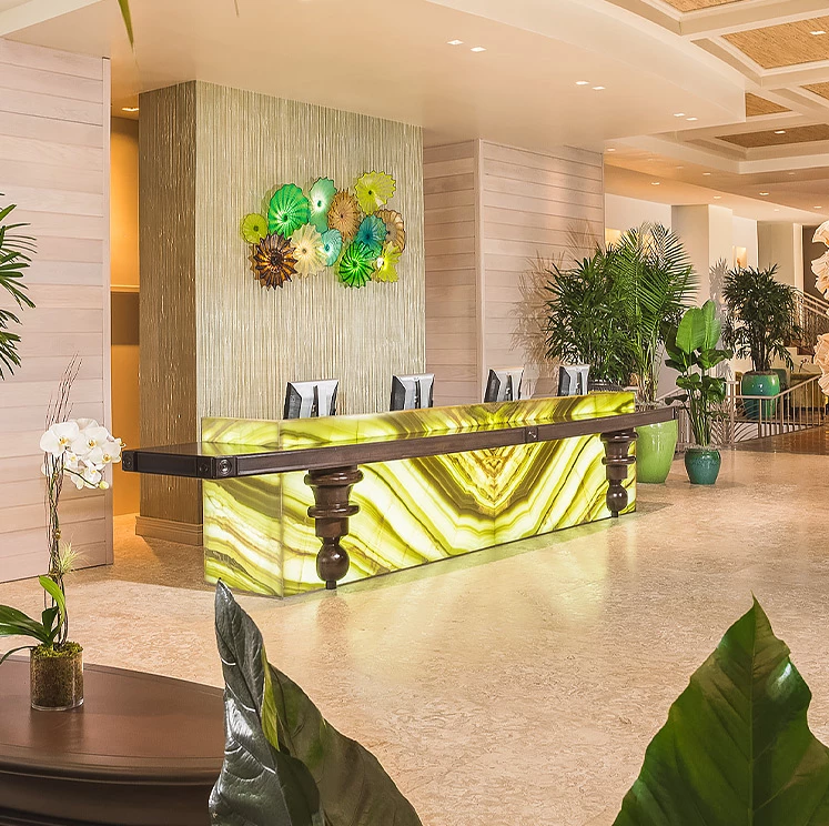 A bright and welcoming hotel lobby with a reception desk, plants, and artwork.