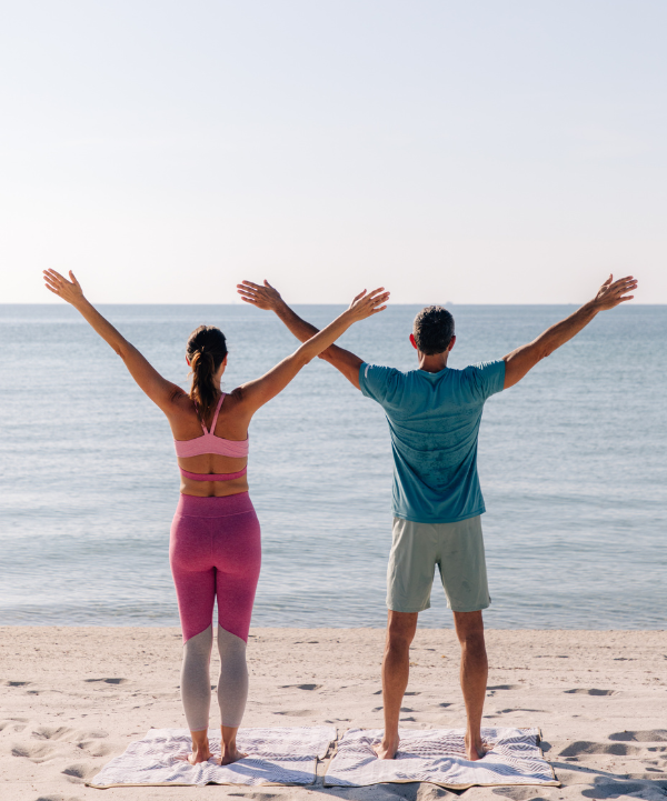 a man and woman standing on a beach with their arms raised