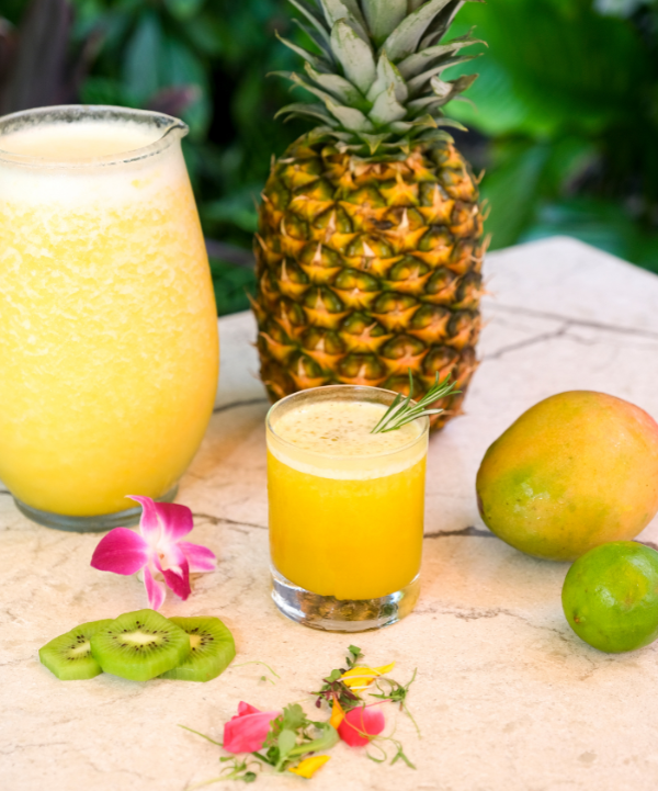 a glass of yellow liquid next to fruit
