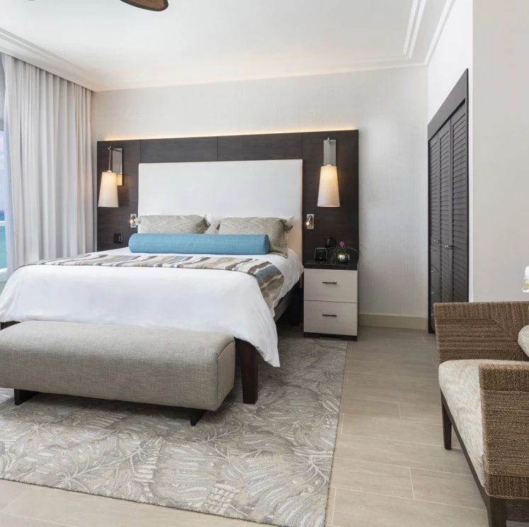 A wide view of a hotel room with a bed, nightstand, chair, and rug.
