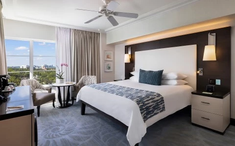 A hotel room with a large bed, nightstands, and a window with a city view.