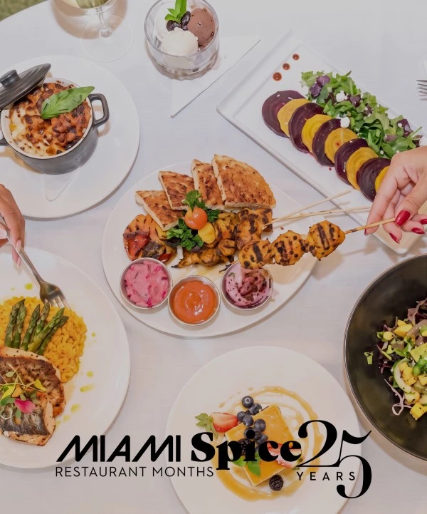 A table set with various dishes of food, including skewers, salads, and bread, with hands holding utensils.