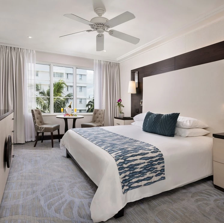 A wide view of a hotel room with a large bed, ceiling fan, and window
