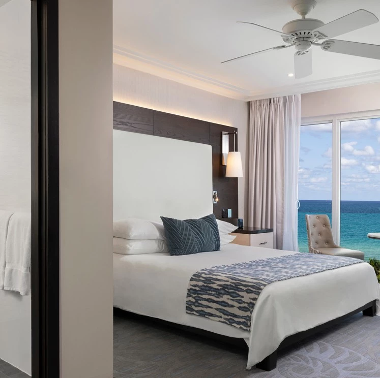A wide view of a hotel room with a large bed, ocean view, and modern furnishings.