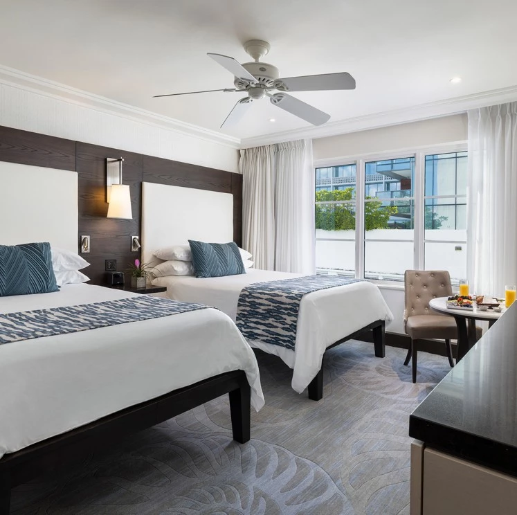 A hotel room with two beds, a desk, and a ceiling fan.