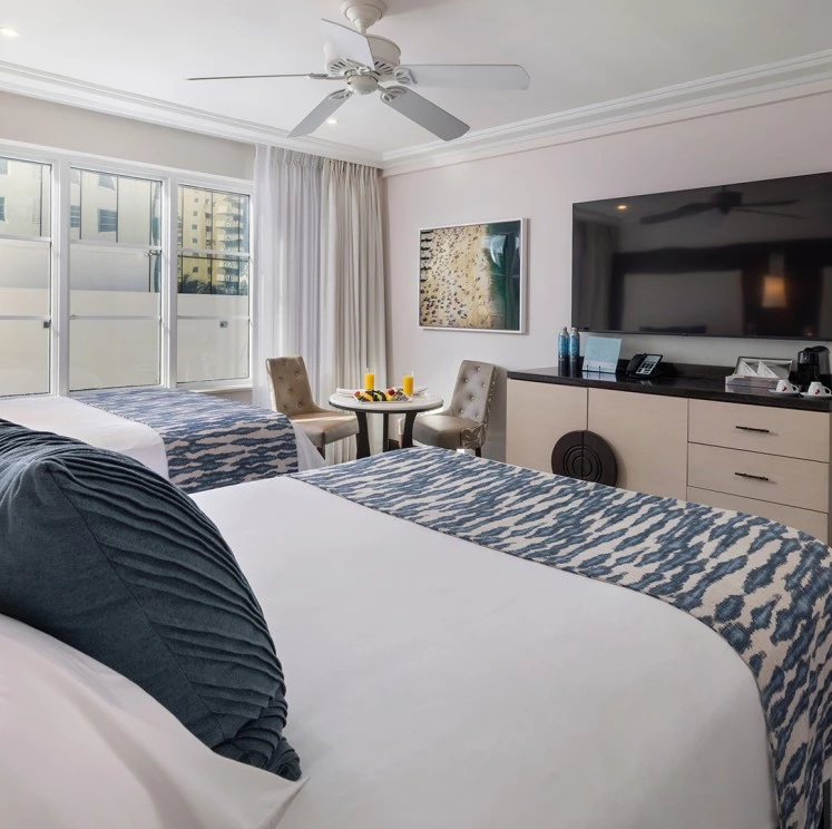 A hotel room with two beds, a large TV, and sliding glass doors