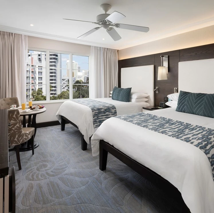 A hotel room with two beds, a table and chairs, and a city view.