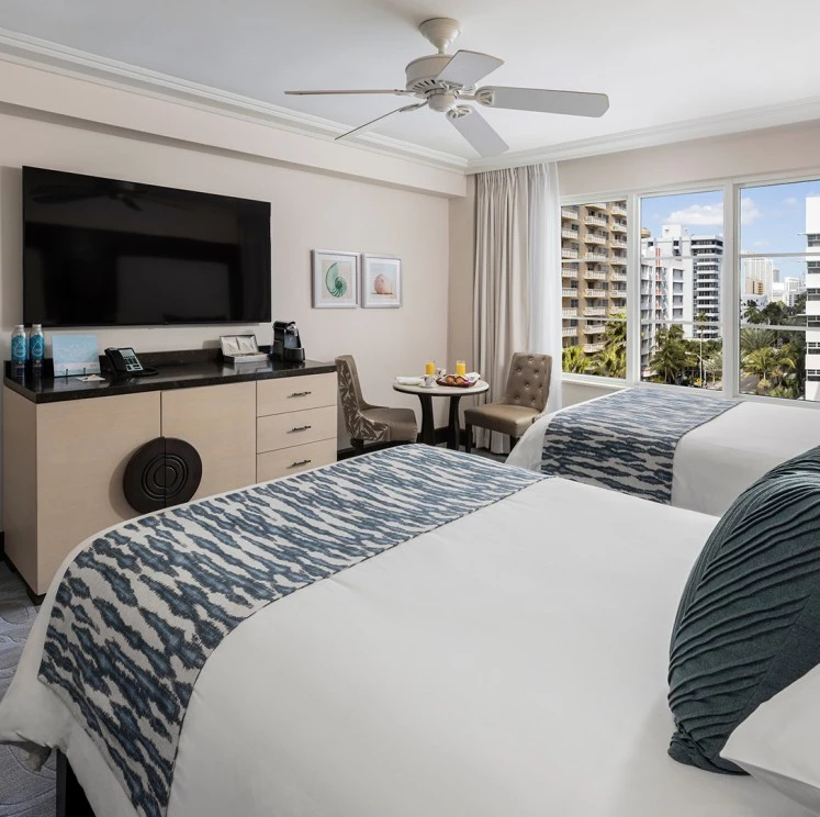A hotel room with two beds, a large TV, and a city view.