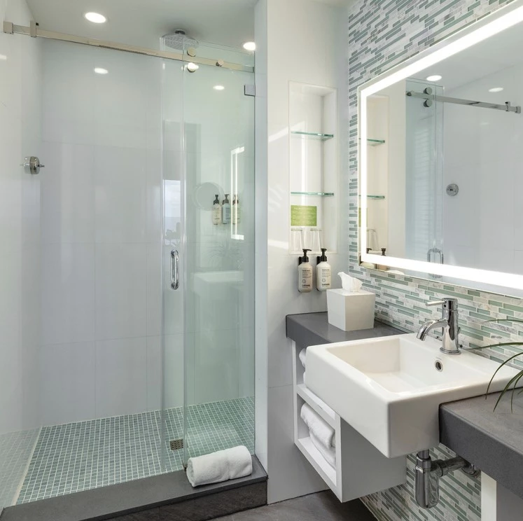 A modern bathroom with a glass-enclosed shower, a single sink, and a large rectangular mirror.