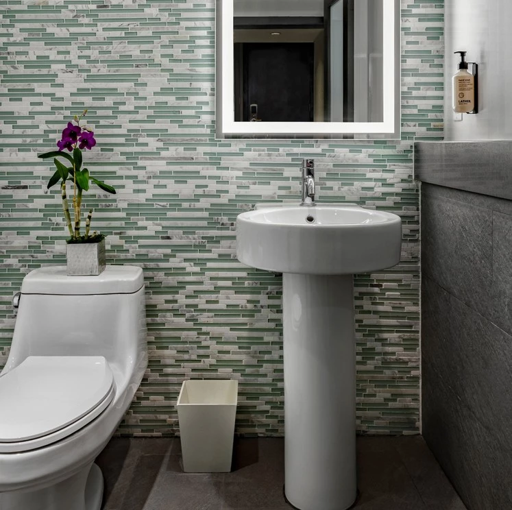 A modern bathroom with a white toilet, pedestal sink, and green tile wall