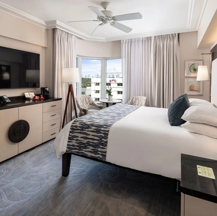 A wide-angle view of a hotel room with a large bed, TV, and window.