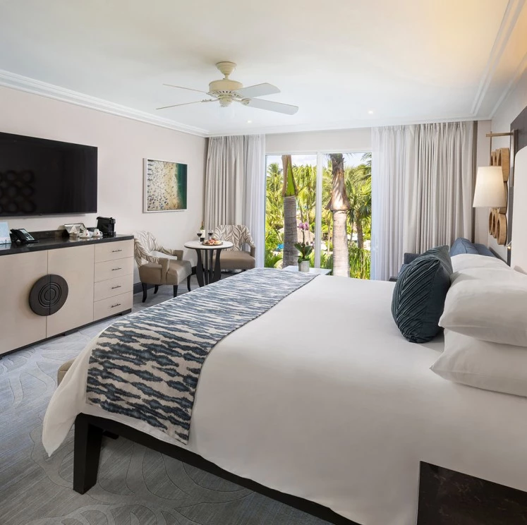 A wide view of a hotel room with a large bed, TV, ceiling fan, and window seating area.