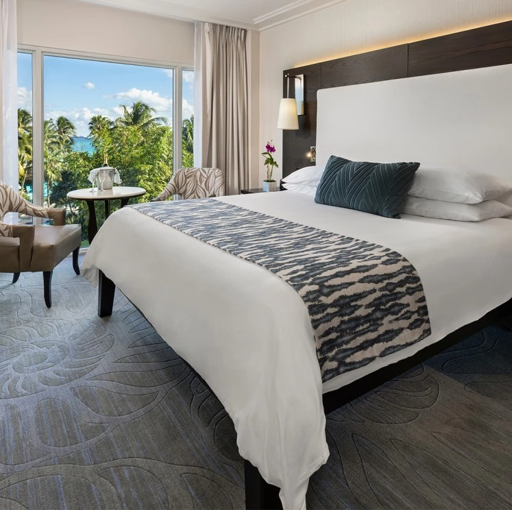 A wide-angle view of a hotel room with a large bed, sitting area, and a view of palm trees outside.