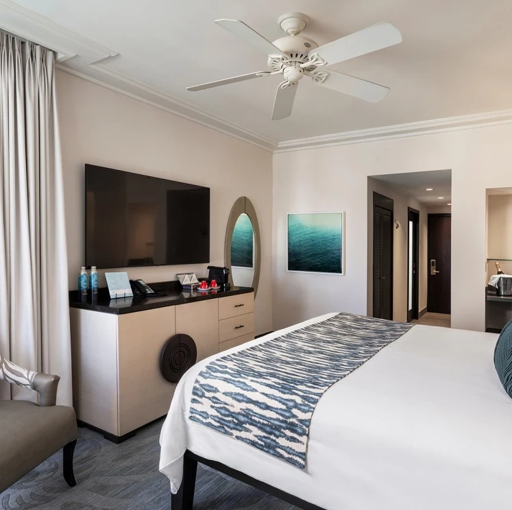 A wide-angle view of a hotel room with a bed, TV, dresser, and chair.