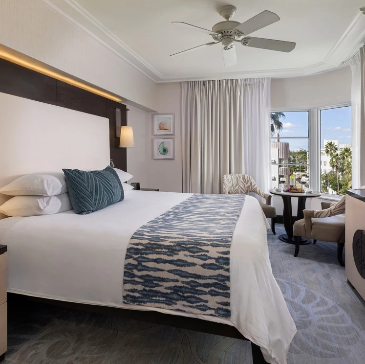 A wide view of a hotel room with a large bed, ceiling fan, and window.