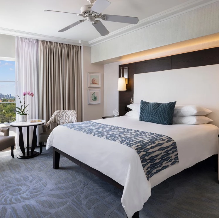 A wide view of a hotel room with a large bed, chair, table, and city view.