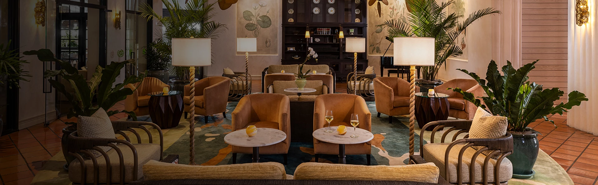 A stylish hotel lobby lounge with comfortable seating, large rug, tiled floor, plants, and lamps.