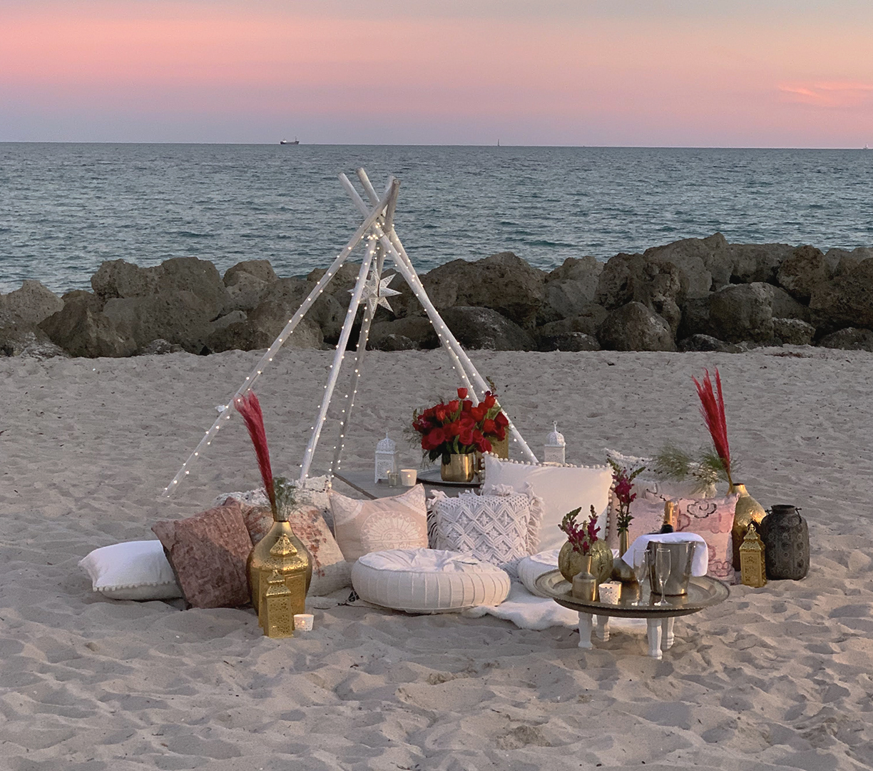 a beach setting with a tent and pillows and flowers