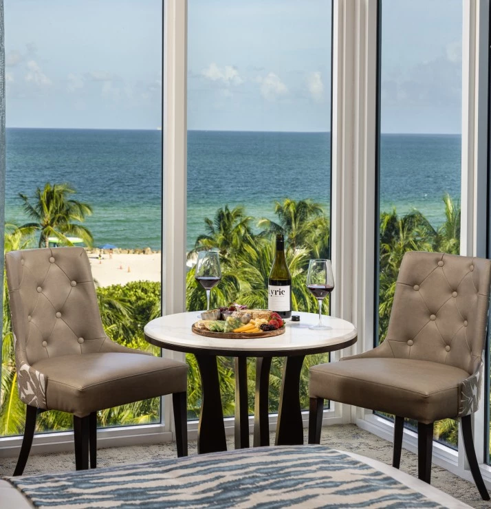 a table with wine glasses and bottles on it by a window with a view of the ocean