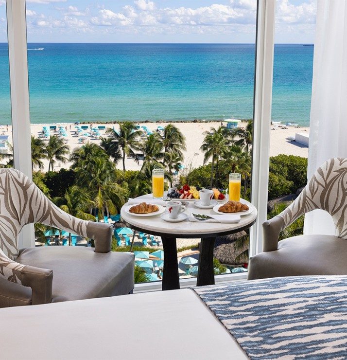 a table with food and drinks on it by a window overlooking a beach